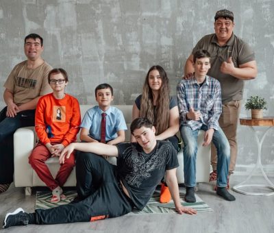 Group of seven people posing casually in a stylish indoor setting with a concrete wall background.