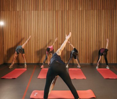 Yoga class with diverse adults stretching on mats in a cozy wooden studio.